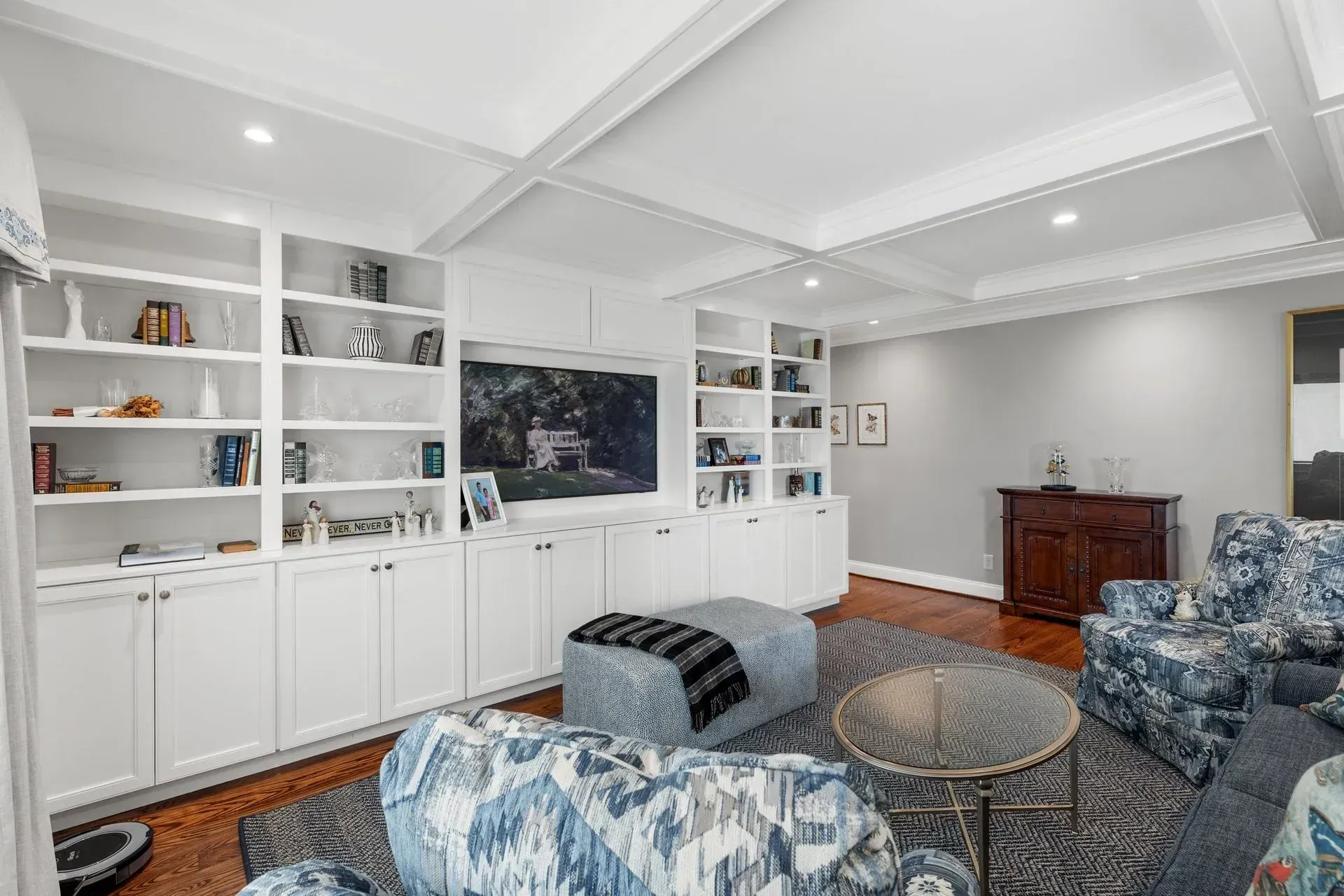 White built-in shelves flank TV in a living room with patterned blue armchairs, ottoman, and coffee table on a rug.