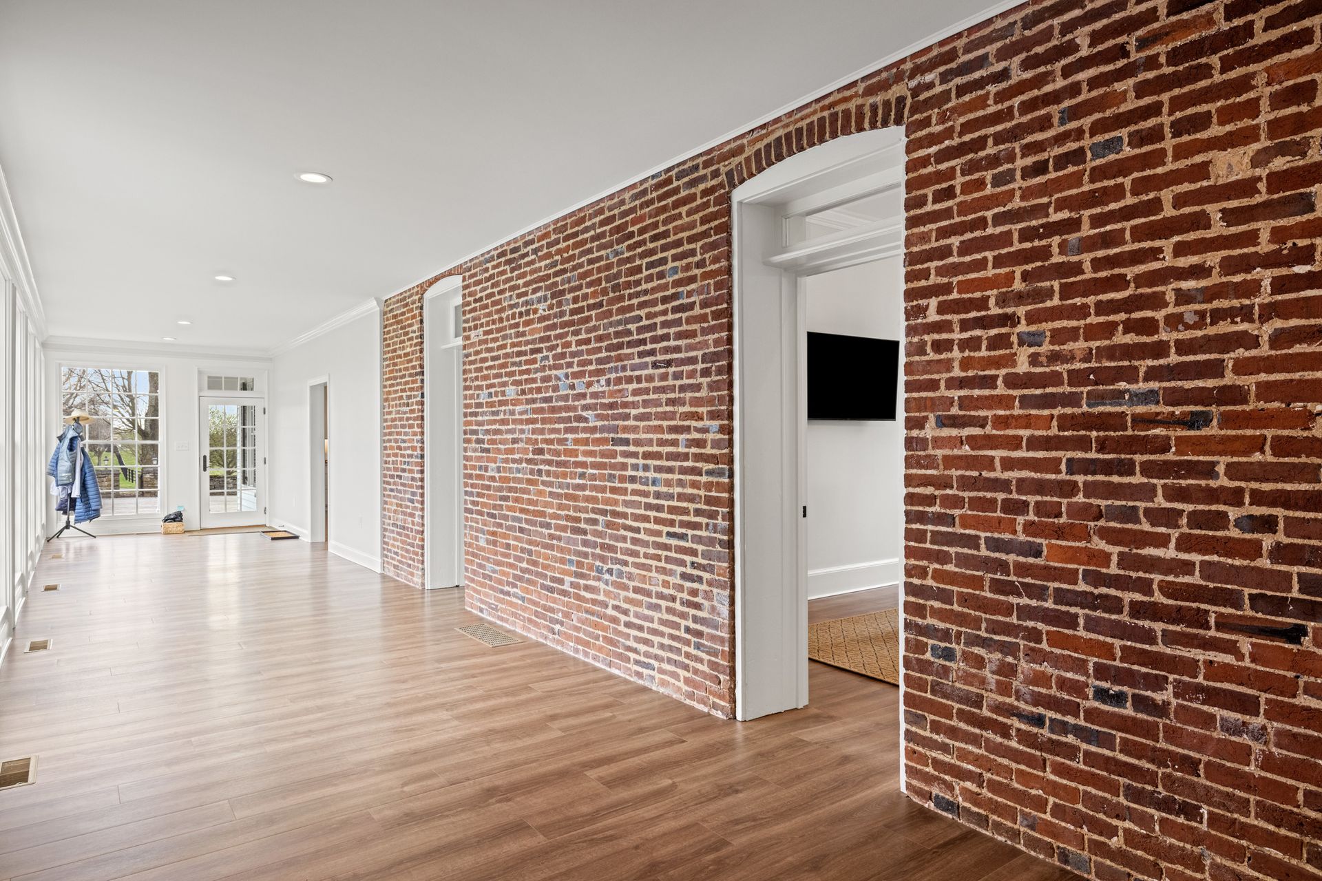 Long, light-filled hallway with brick accent walls and hardwood floors.
