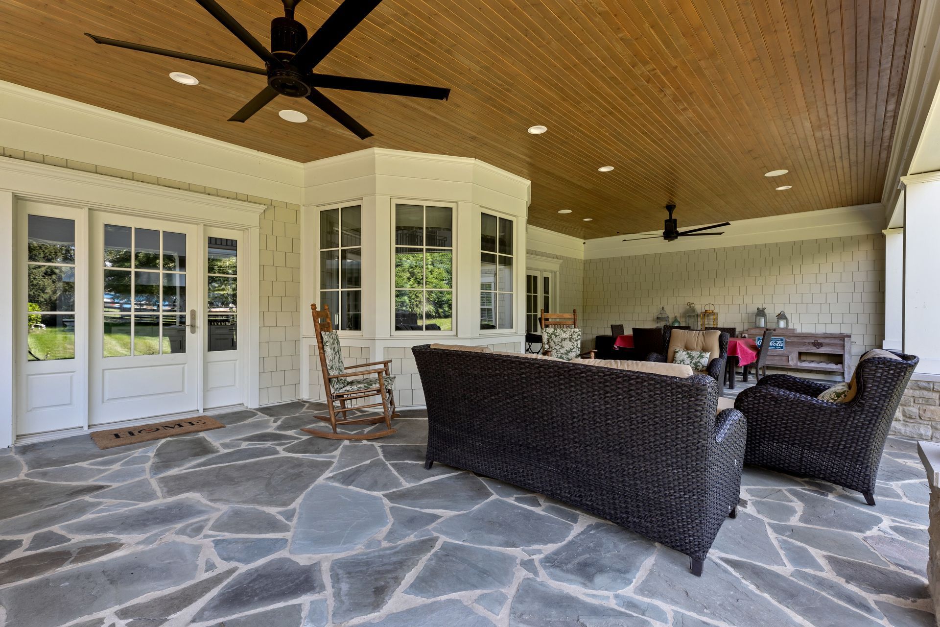 Covered patio with gray stone floor, wicker furniture, and bay window.
