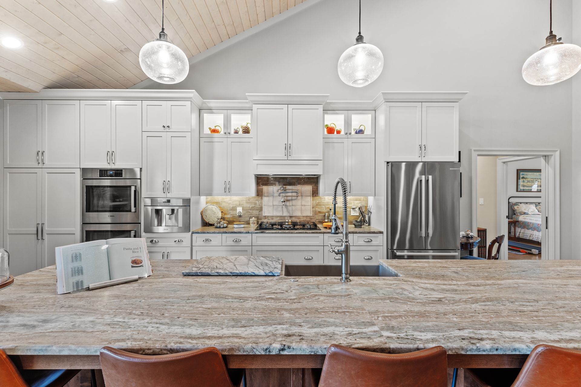White kitchen with island, stainless steel appliances, and pendant lights.