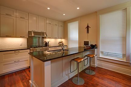 Cream-colored kitchen with dark countertops, stainless steel appliances, and hardwood floors.