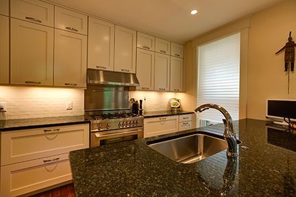 Cream-colored kitchen cabinets and dark granite countertops. Stainless steel appliances. Island with sink.