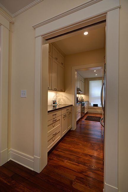 Narrow kitchen hallway with wooden floors, cabinetry, and doorway to a kitchen.