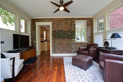 Living room with brick accent wall, brown leather chairs, and hardwood floors.