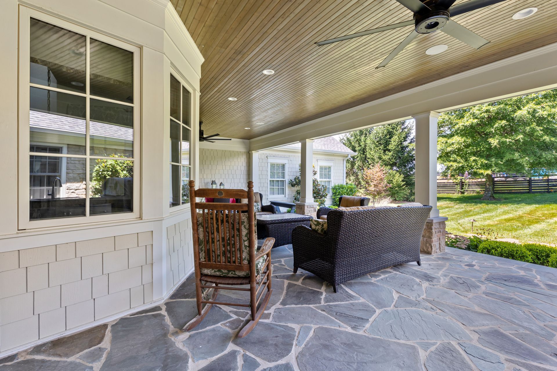 Covered patio with stone floor, wicker furniture, and a wooden rocking chair.