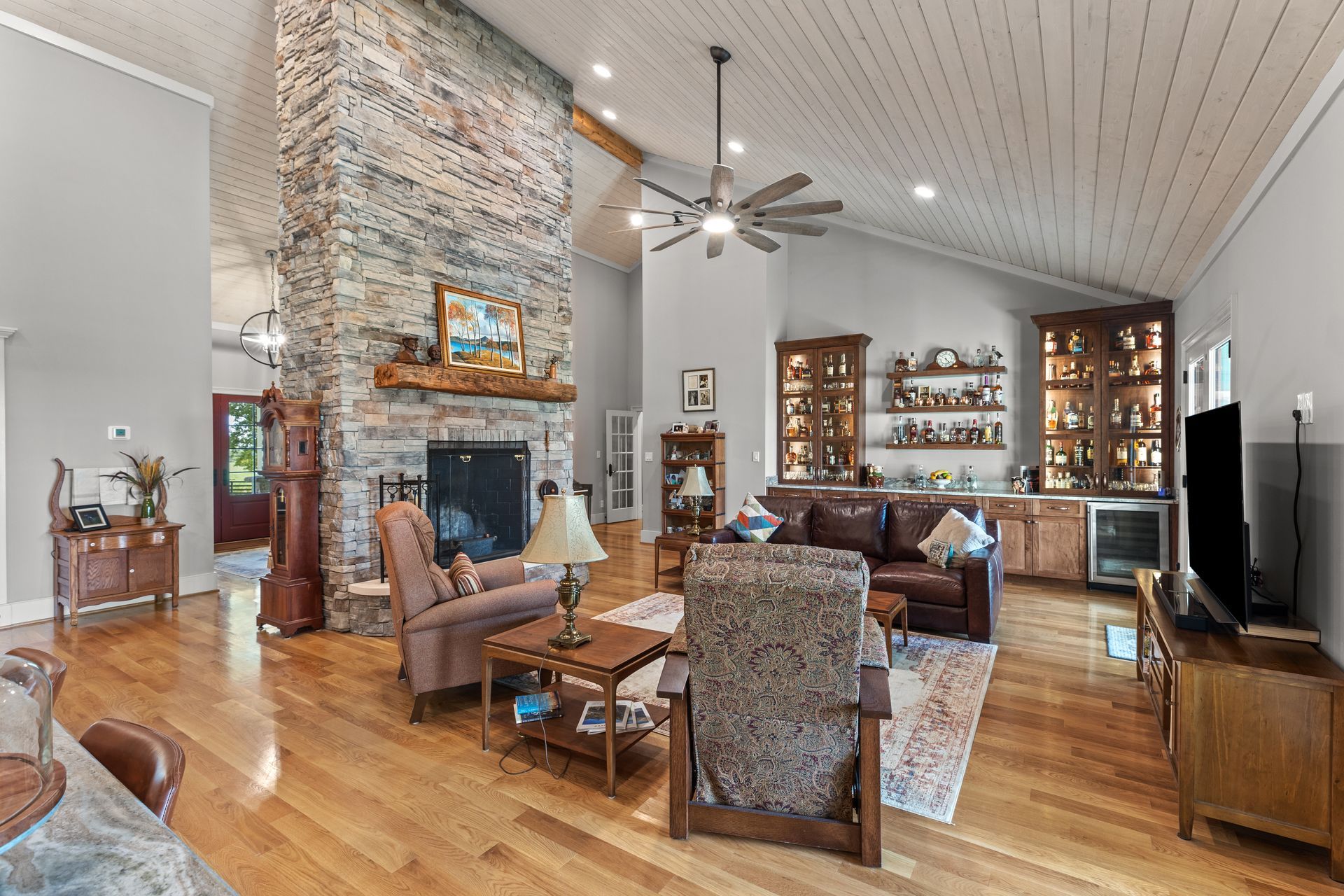 Spacious living room with stone fireplace, wood floors, and built-in bar.