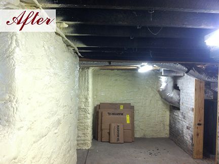 Basement interior after insulation. Walls are coated in white foam, exposed beams, and cardboard boxes.