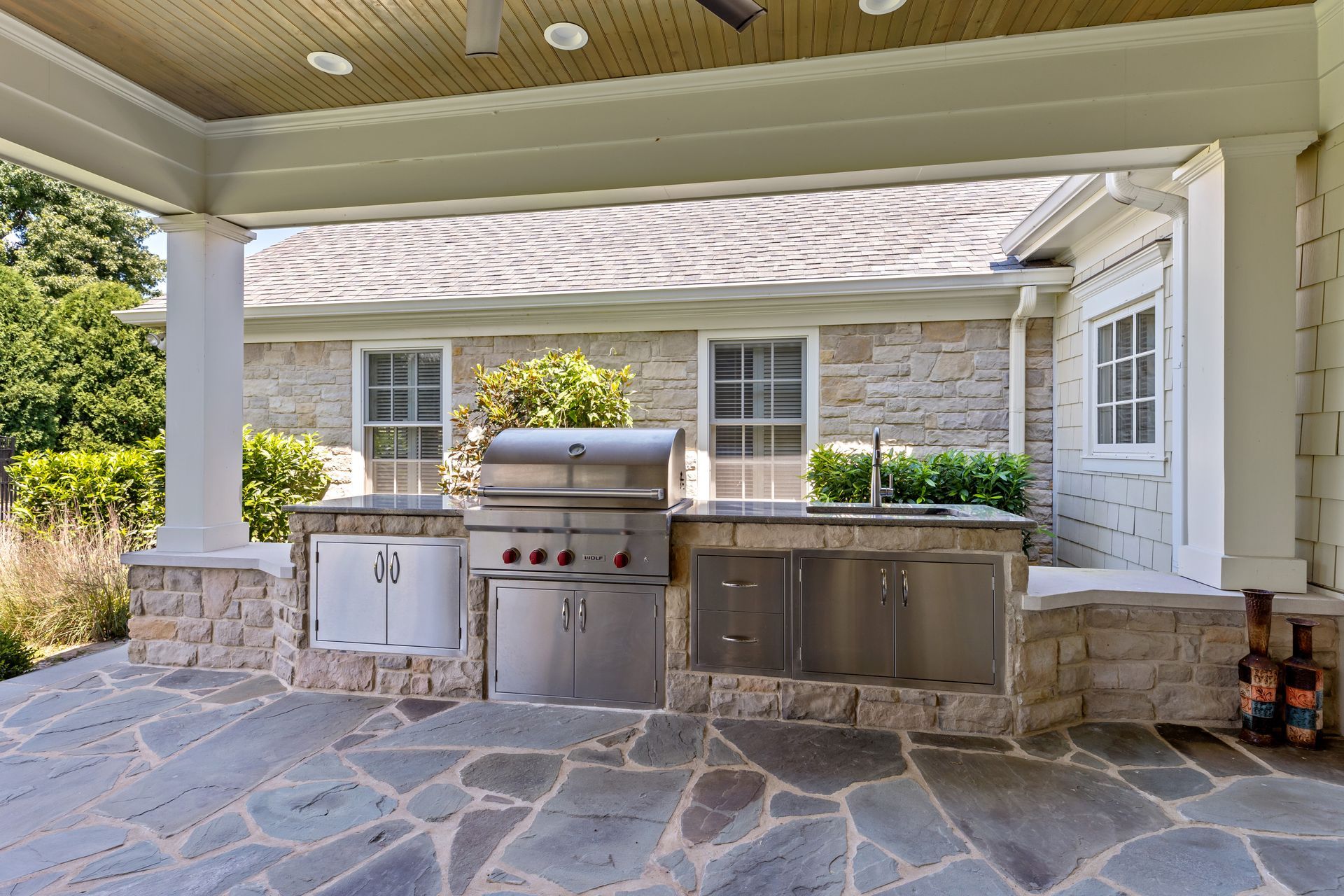 Outdoor kitchen with stainless steel appliances, stone facade, and flagstone patio.