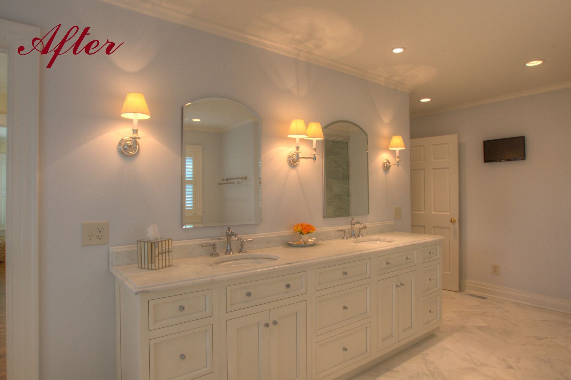Bathroom with white vanity, marble countertop, arched mirrors, sconce lighting, and a door.