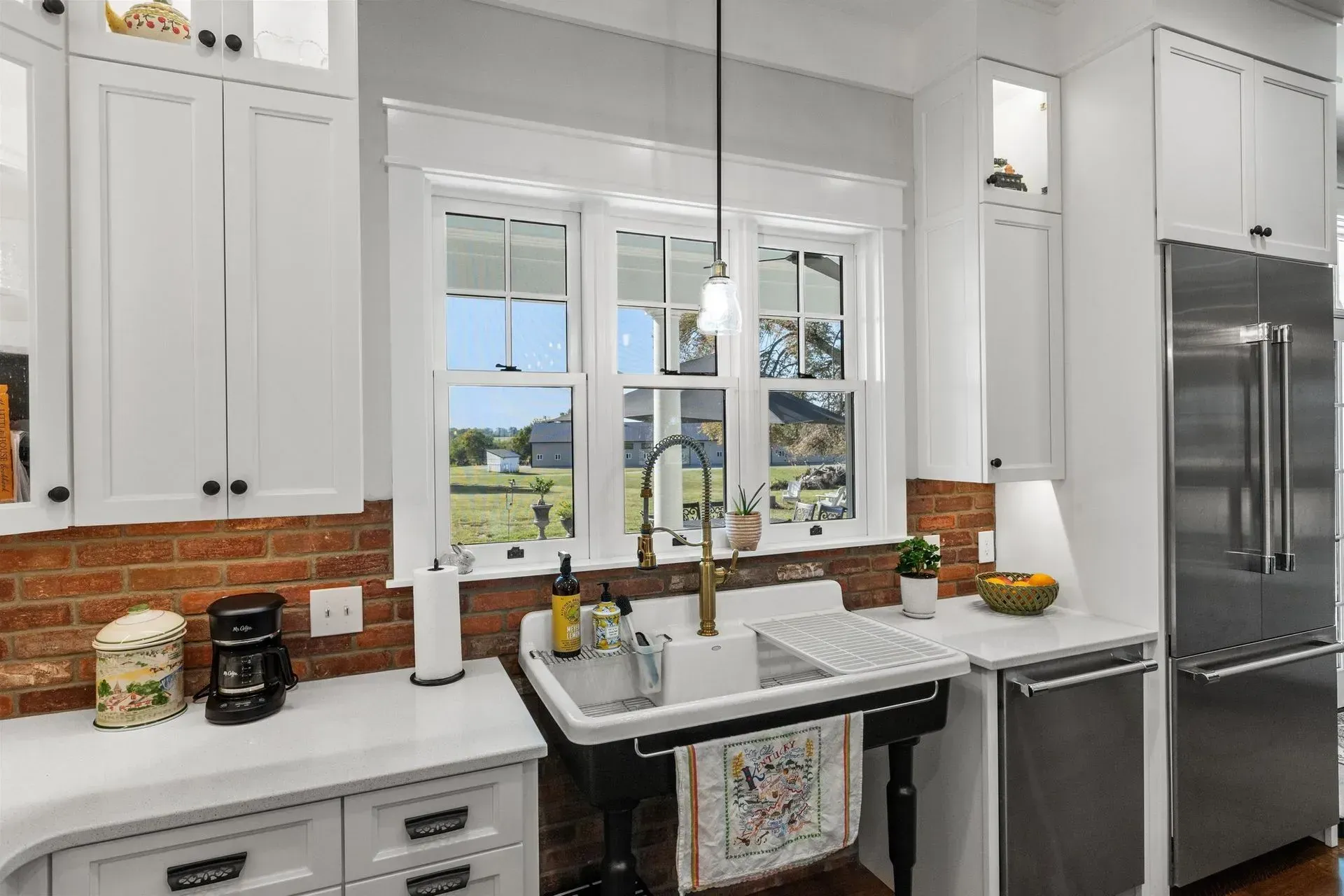 White kitchen with a farmhouse sink, brick backsplash, and stainless steel appliances.