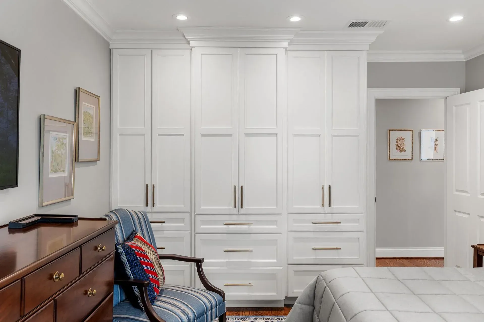 White built-in wardrobe in a bedroom with a dresser and a chair.