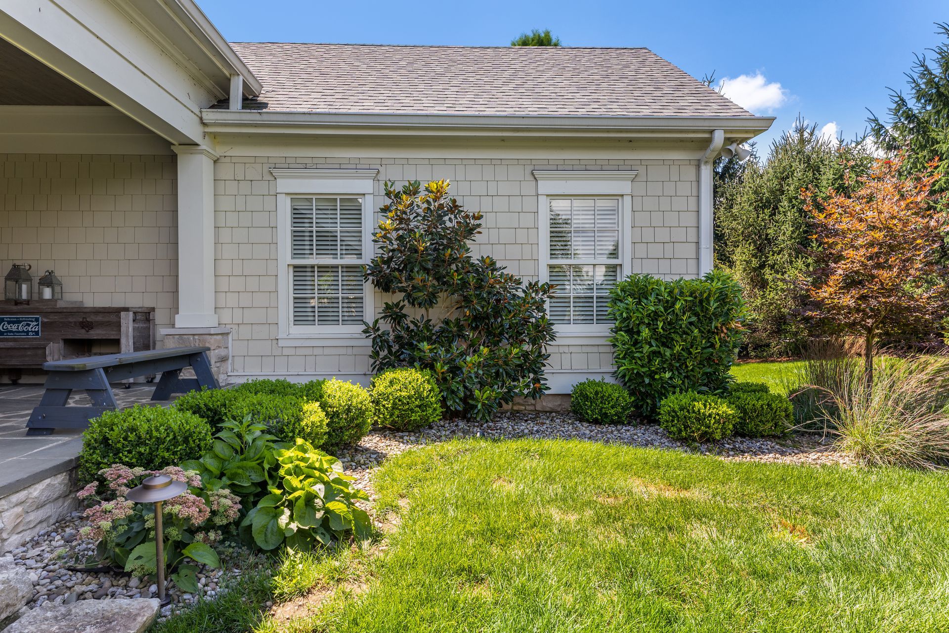 Exterior view of a light-colored house with white windows, surrounded by a green lawn and landscaping.