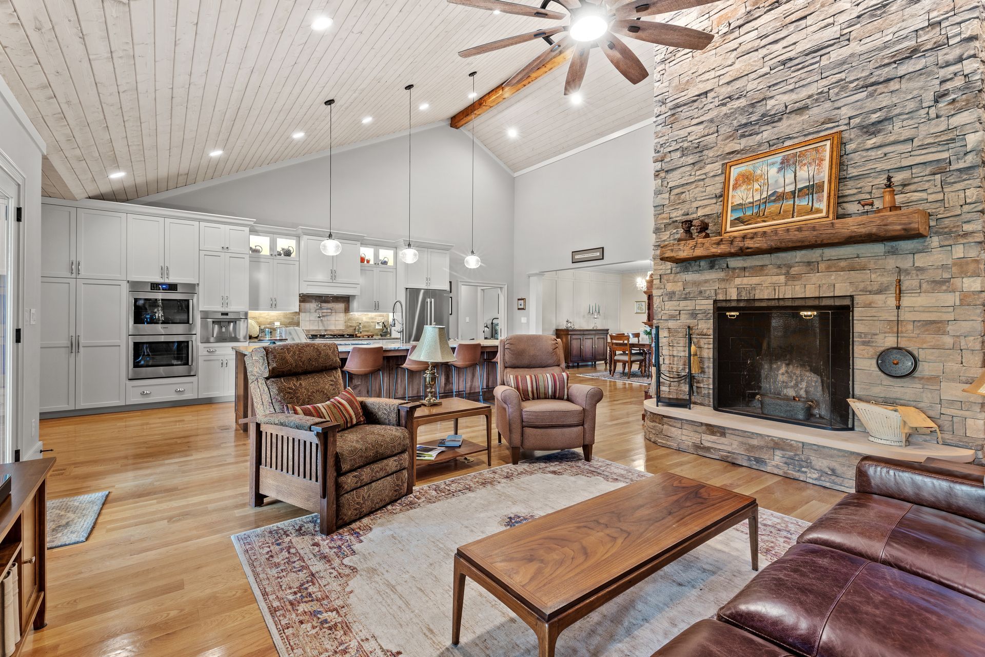 Spacious living room with stone fireplace, open kitchen, and wood ceiling.