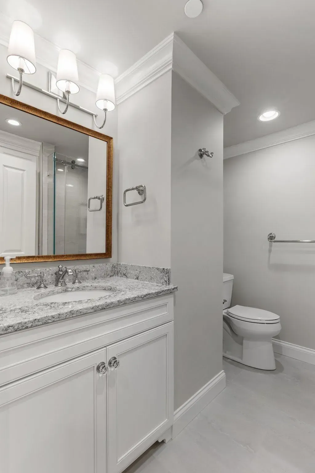 Bathroom with white vanity, countertop, mirror, and toilet; light gray walls and flooring.