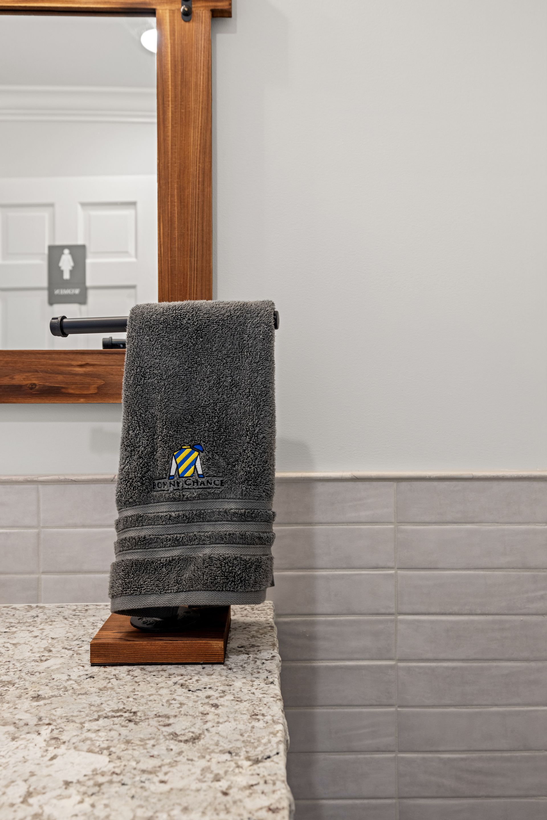 A dark gray towel on a wooden rack in a bathroom. White and gray tiled wall and mirror.