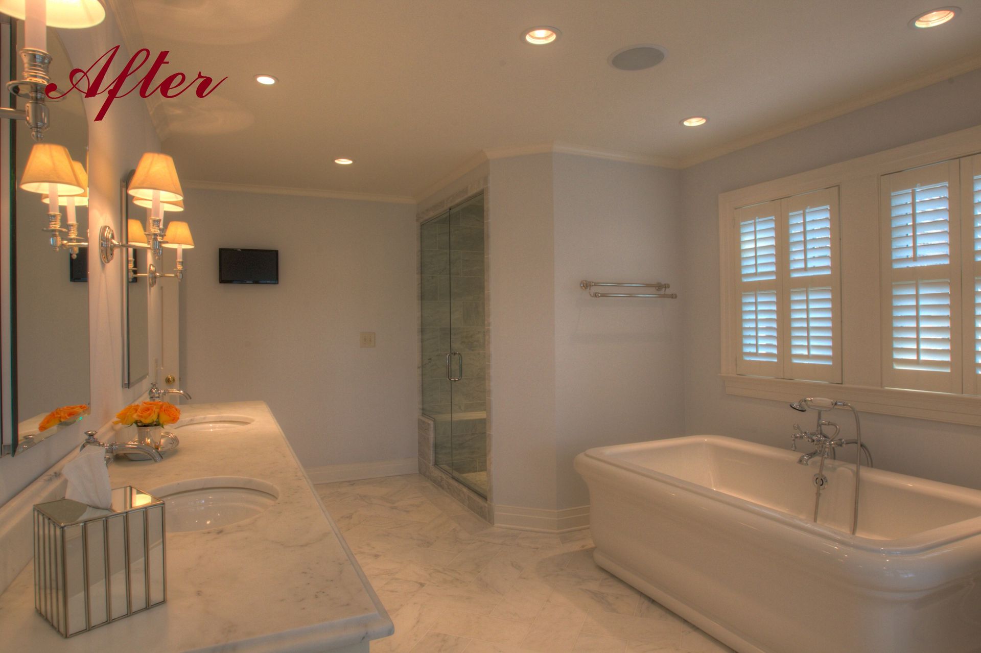 Spacious, well-lit bathroom with double sinks, a tub, shower, and shuttered window.