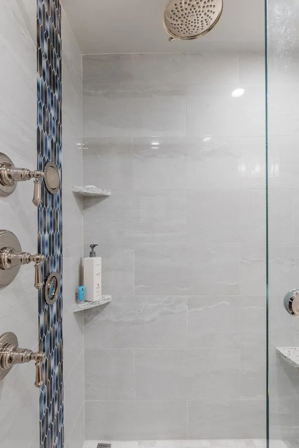 Modern shower with glass door, grey tile walls, mosaic accent, and brushed nickel fixtures.