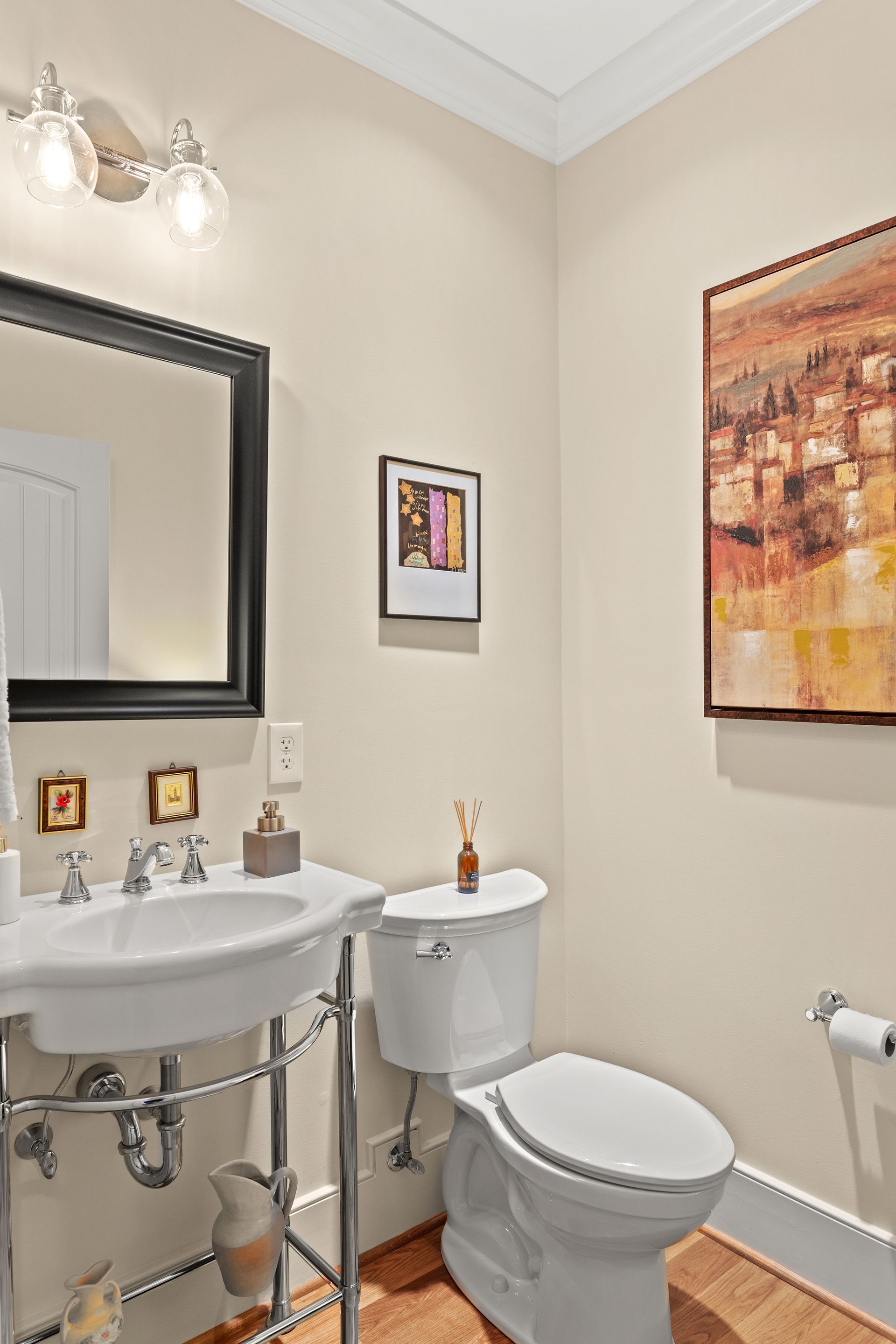 Small bathroom with white fixtures, a pedestal sink, and artwork on the wall; light beige walls.
