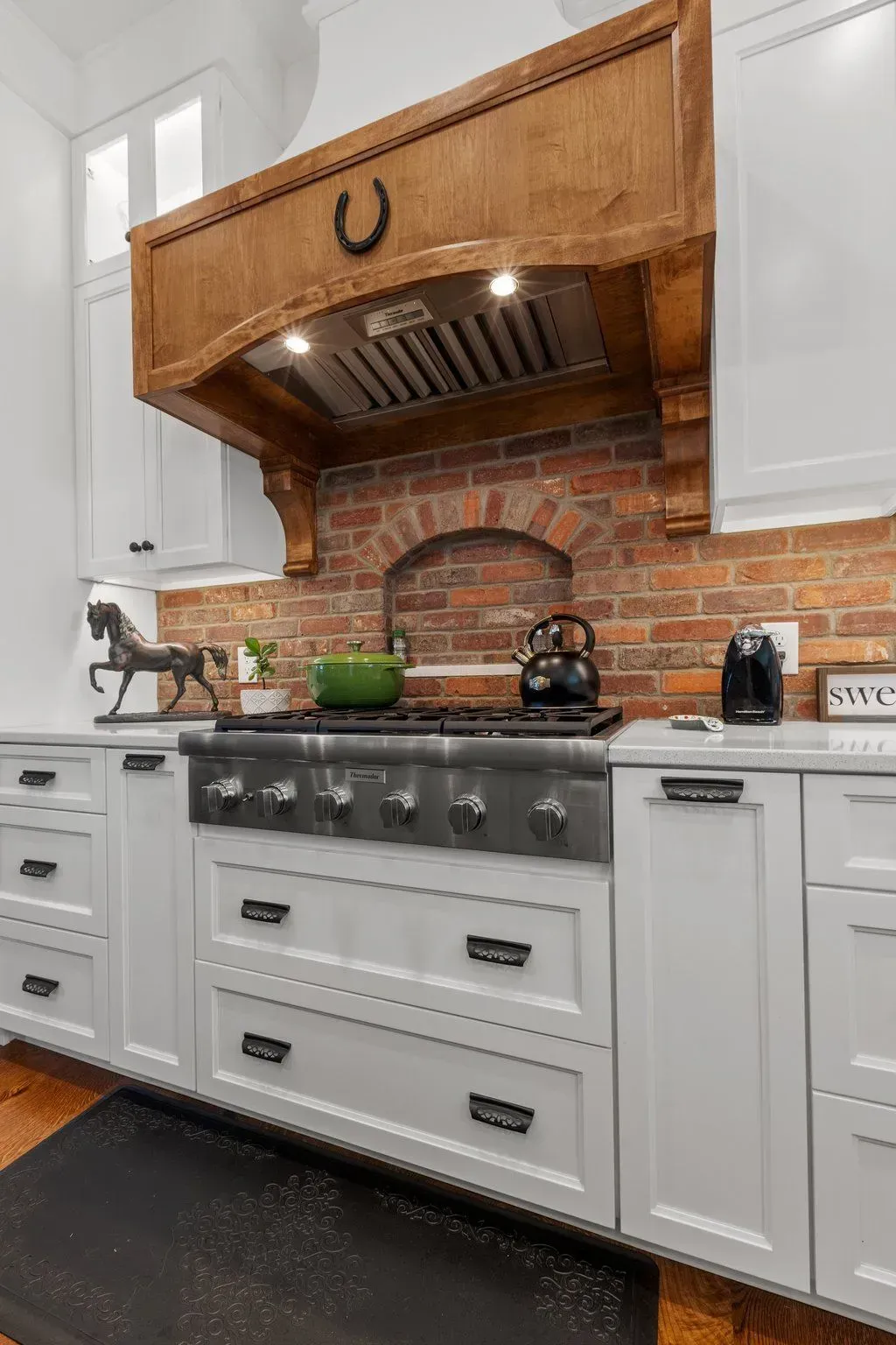 Kitchen with white cabinets, brick backsplash, wooden range hood, and stainless steel stove.