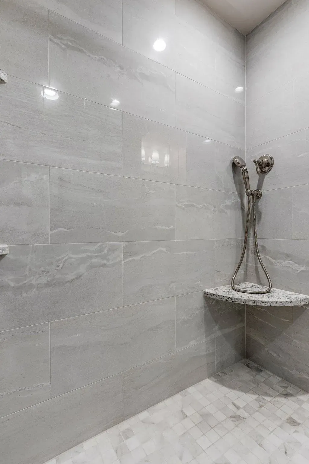 Gray tiled shower with a built-in shelf, a decorative shower fixture, and overhead lights.