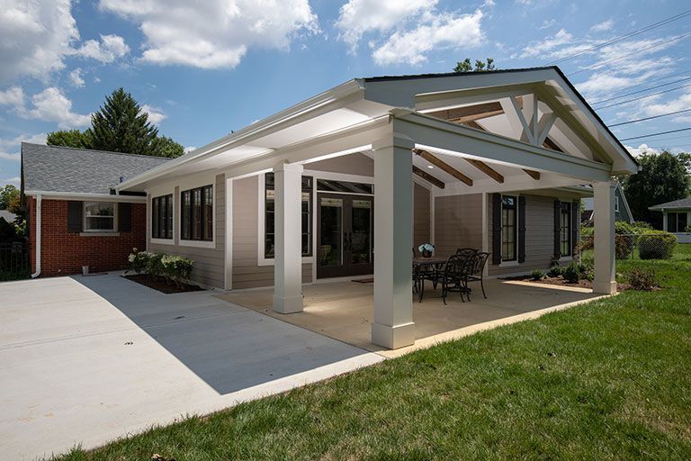 House with a covered patio, light siding, concrete walkway, green grass, and a blue sky.