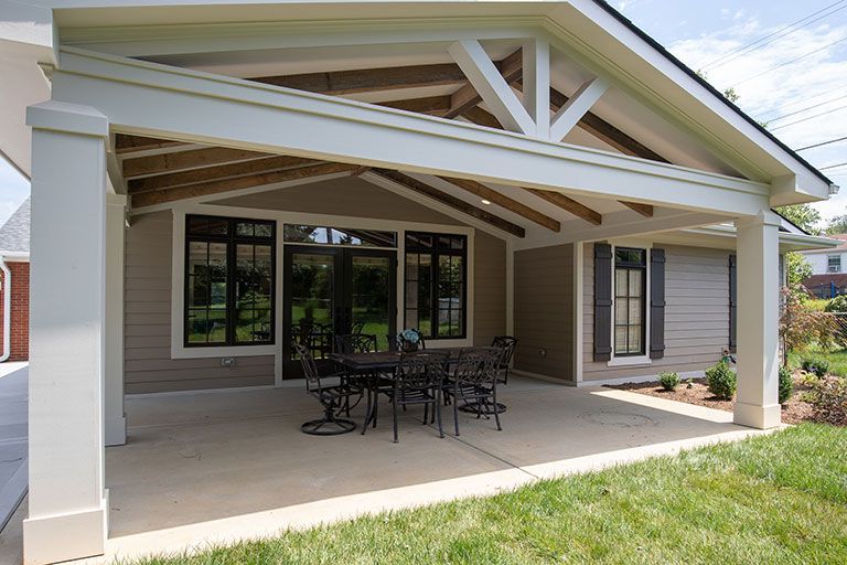 Covered patio with a dining table set on concrete; beige house, green grass.