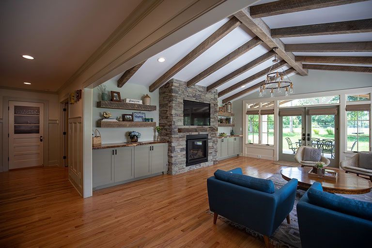 A modern living room with wooden beams, a stone fireplace, and blue armchairs.