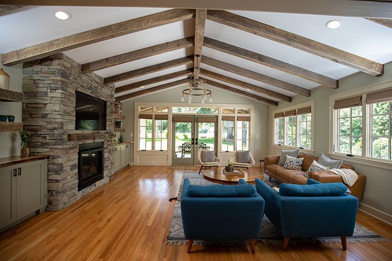 Living room with exposed beams, stone fireplace, teal chairs, and wood floors.