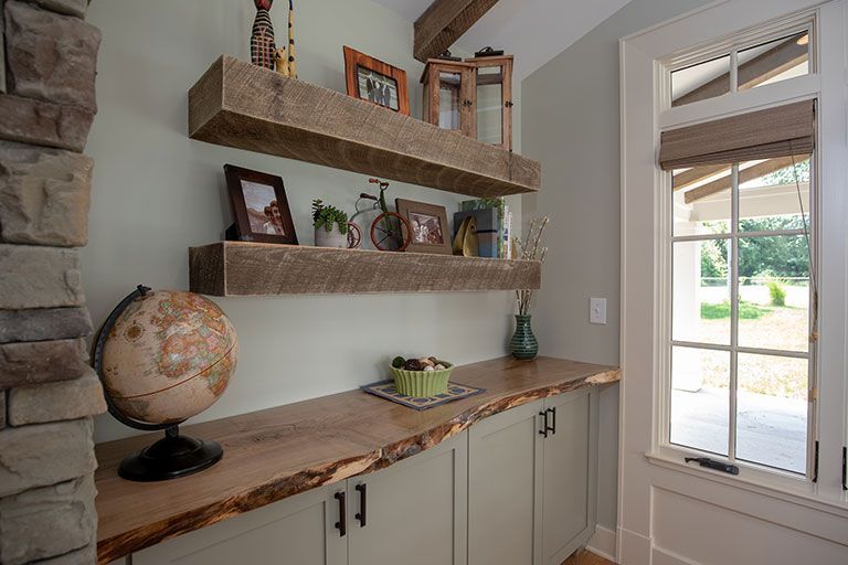 Built-in desk with live edge top, floating shelves, and a stone column next to a window in a room with sage green walls.
