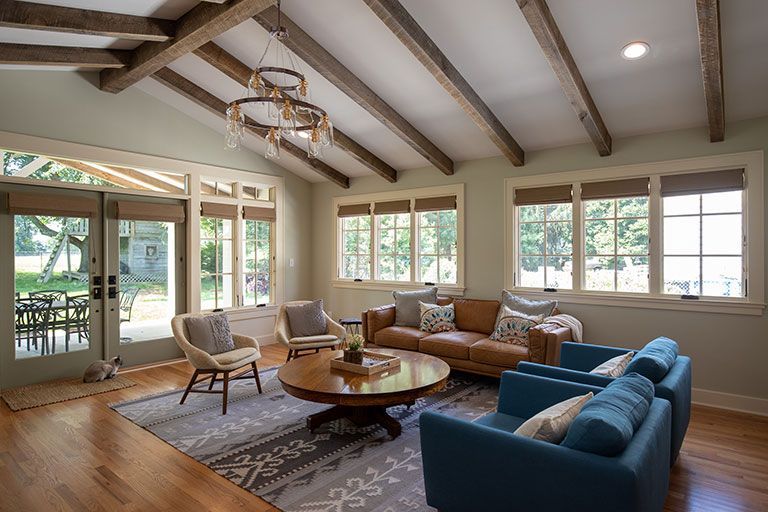 Living room with exposed wooden beams, leather sofa, blue chairs, and large windows.
