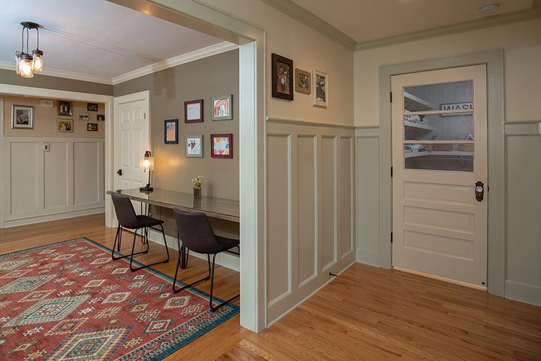 Interior view of a home office with a desk, chairs, art, and a patterned rug. Beige and tan tones.