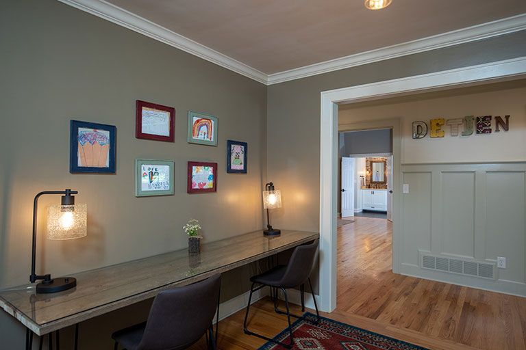 Home office with desk, chairs, and art on wall. View to other room with “DESIGN” letters.