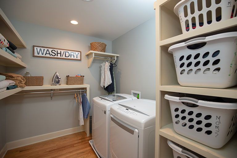 A bright, organized laundry room with washing machine and dryer, shelving, and laundry baskets.