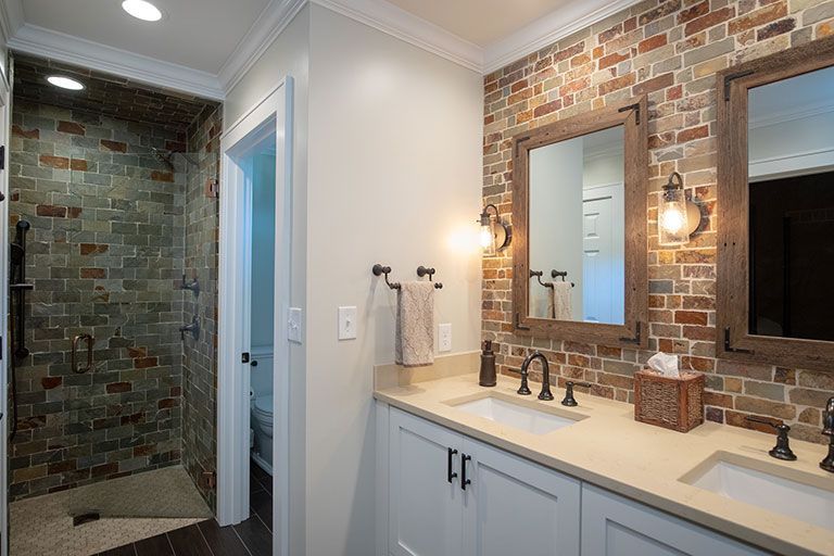 Bathroom with brick accent wall, dual sinks, framed mirrors, and a glass shower.