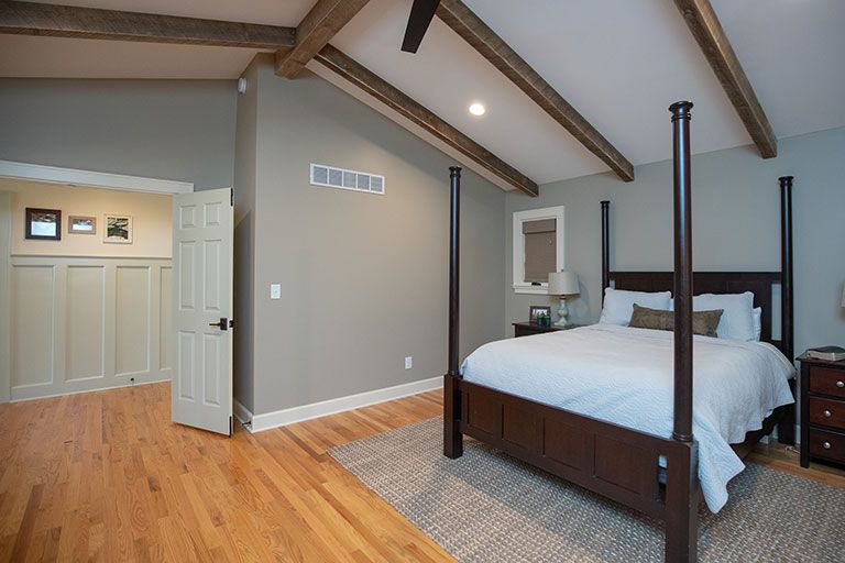 Bedroom with wood floors, a bed, wood ceiling beams, and a doorway.