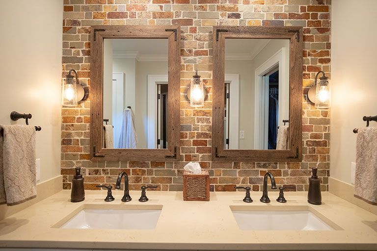 Bathroom with two sinks, brick backsplash, wooden-framed mirrors, and sconce lighting.