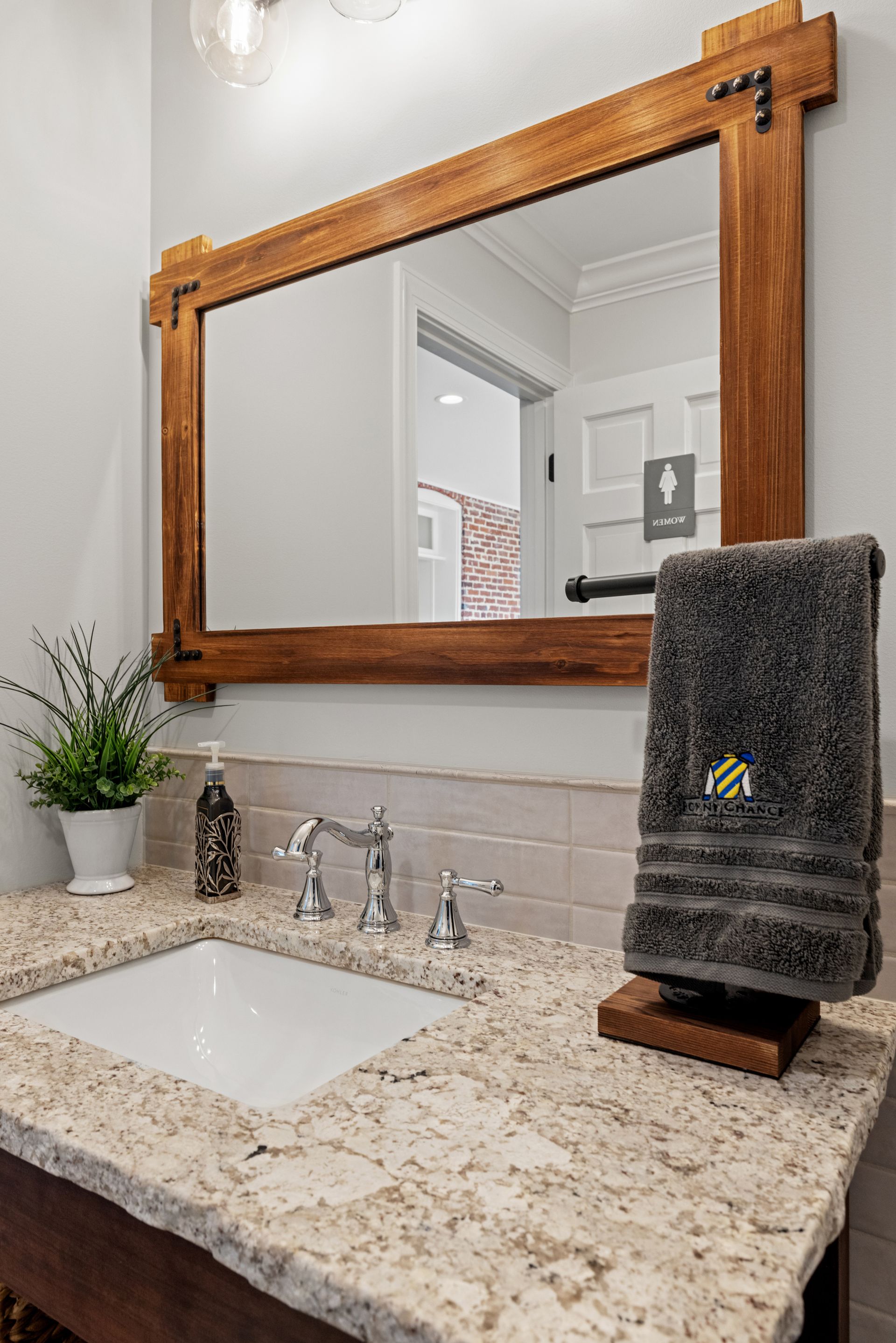 Bathroom vanity with wooden-framed mirror, stone countertop, white sink, and a towel on a stand.