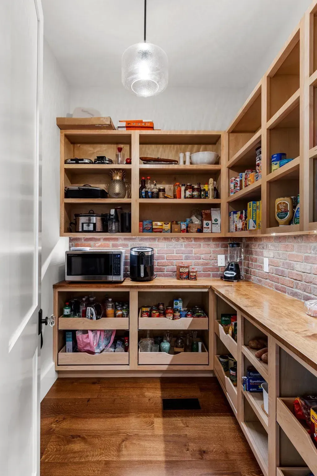 Pantry with wooden shelves, brick accent wall, microwave, and various food items.