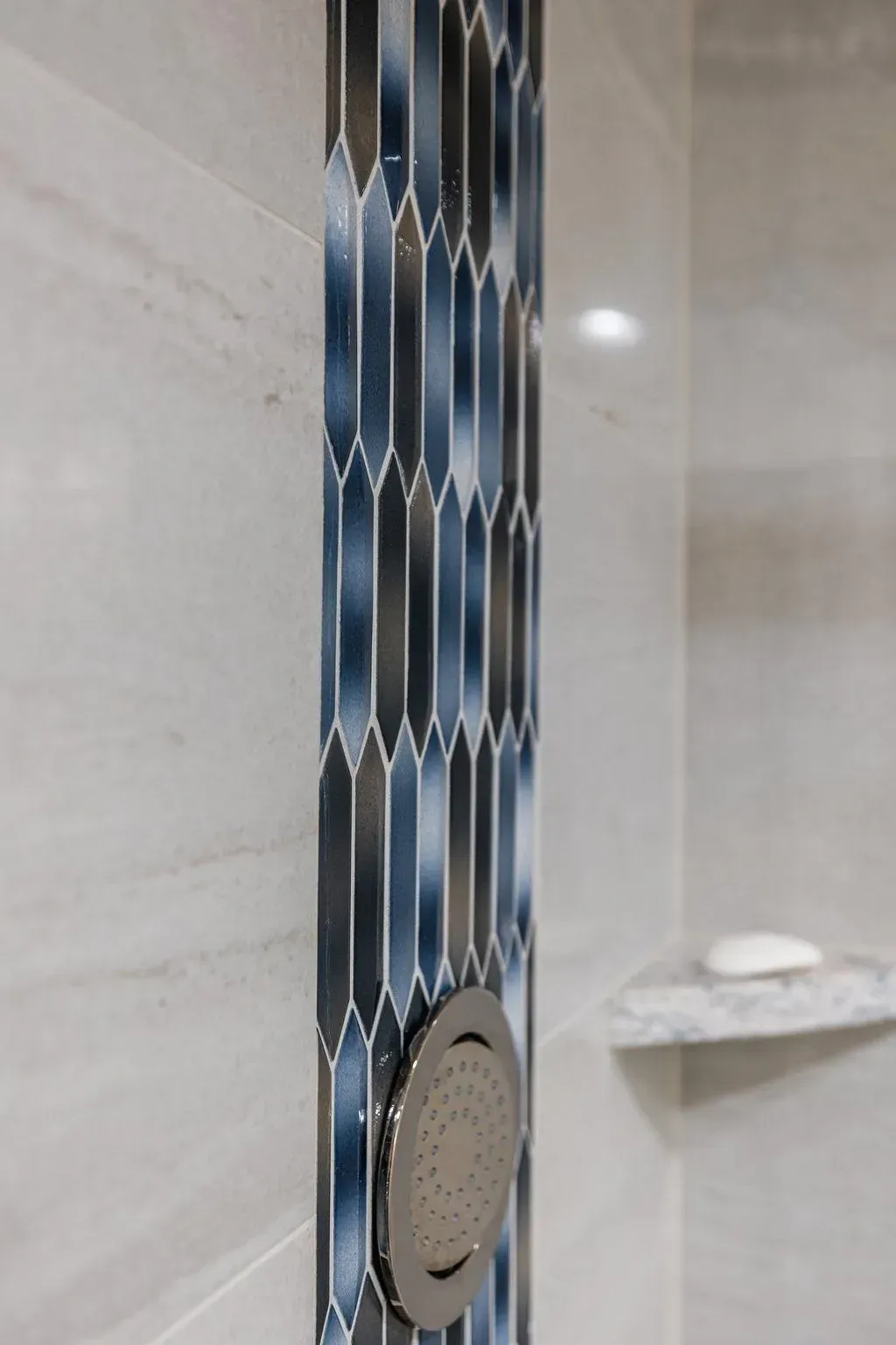 Shower wall with a vertical band of blue and gray patterned tiles, and a round silver showerhead.