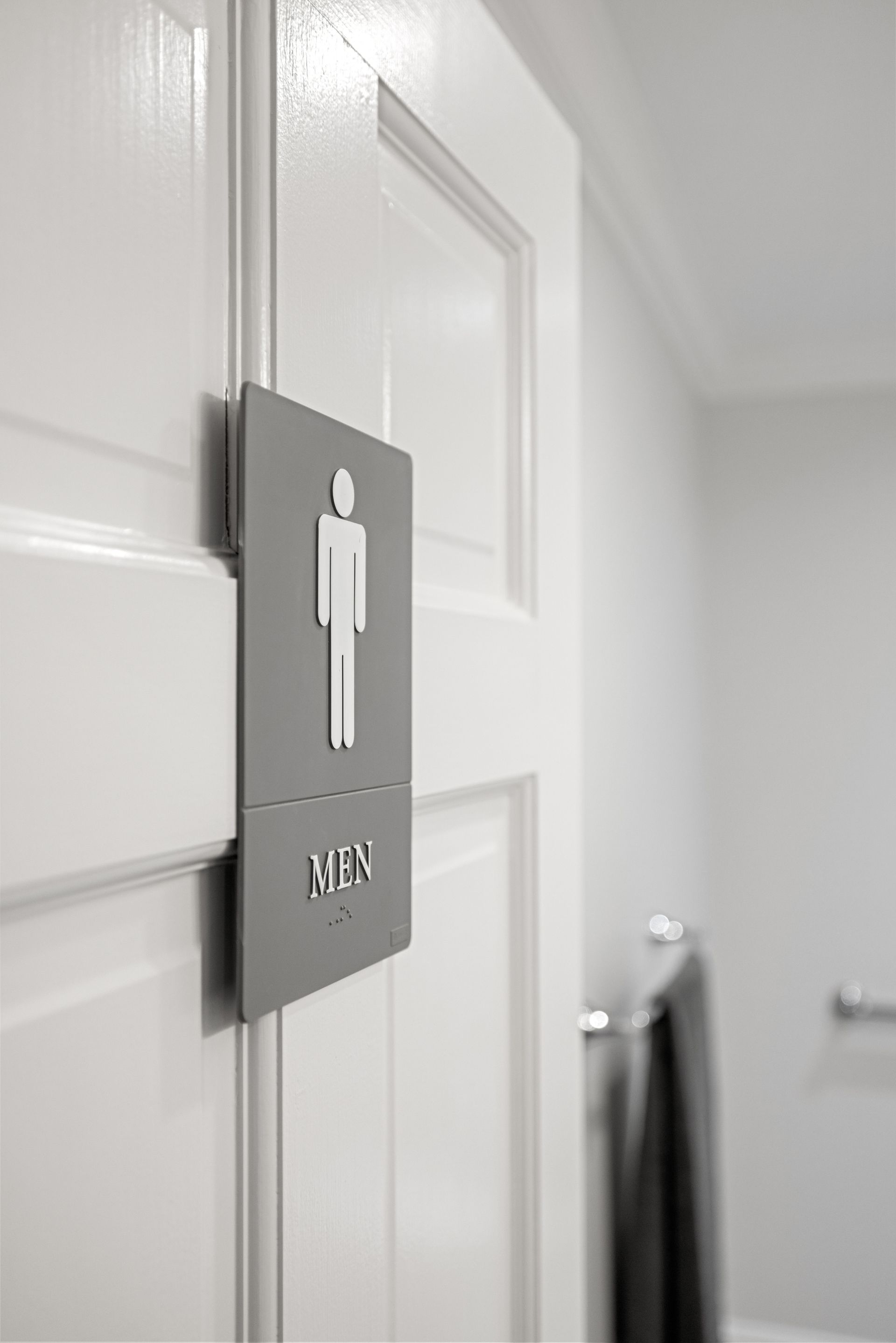 Gray men's restroom sign with braille on a white door.