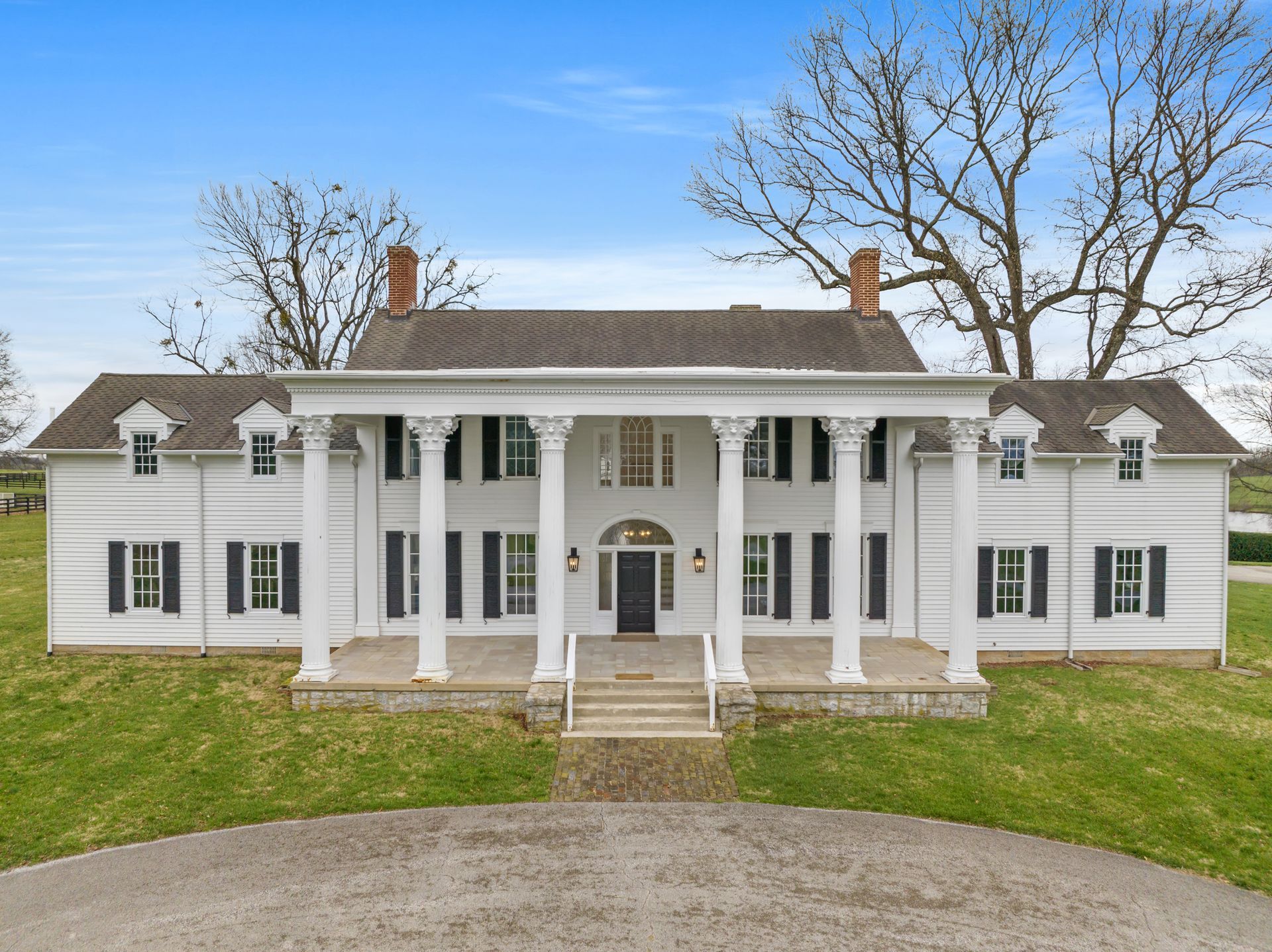 White, two-story mansion with large columns and black shutters, in a grassy field.