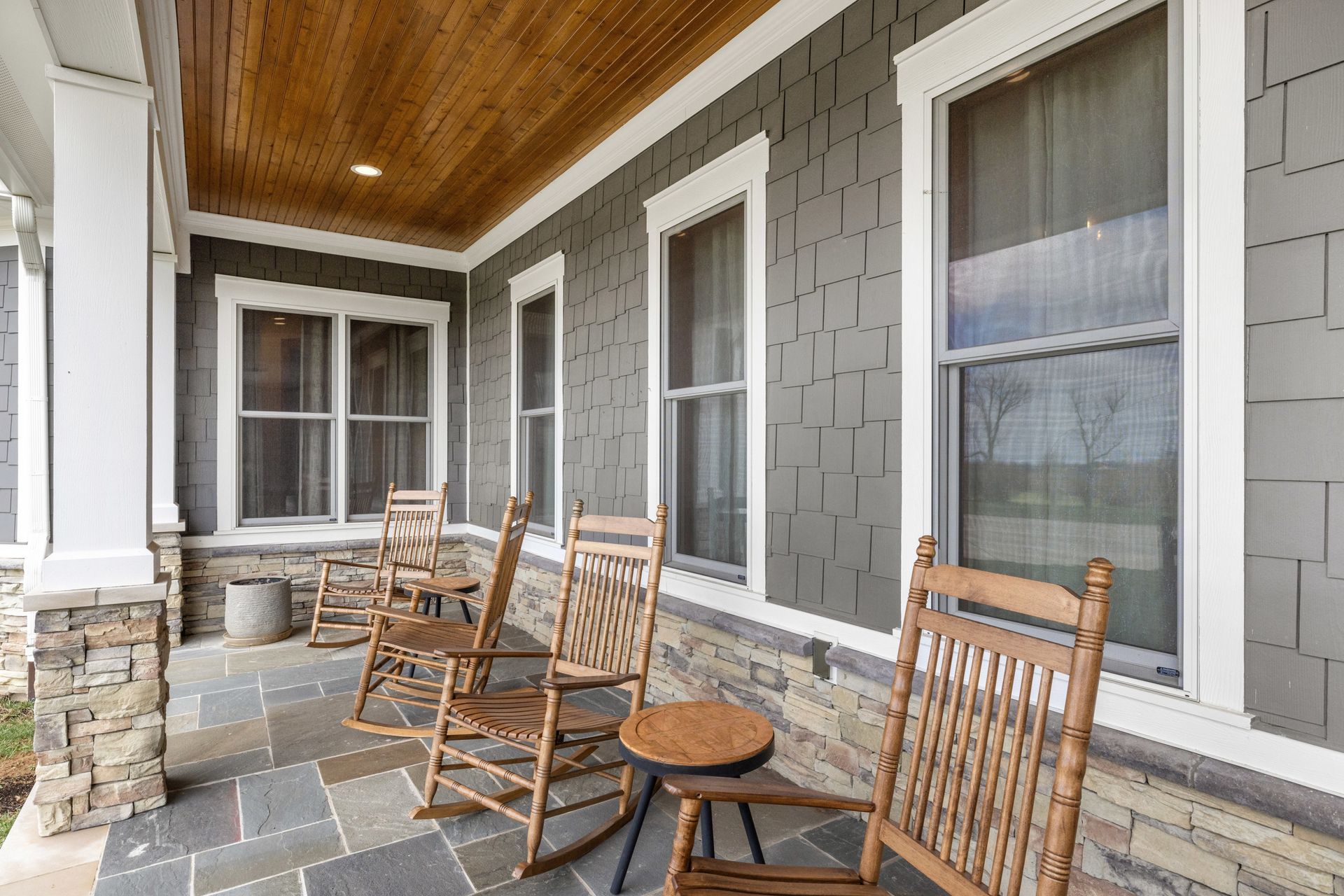 Front porch with rocking chairs, gray siding, and stone columns and accents.