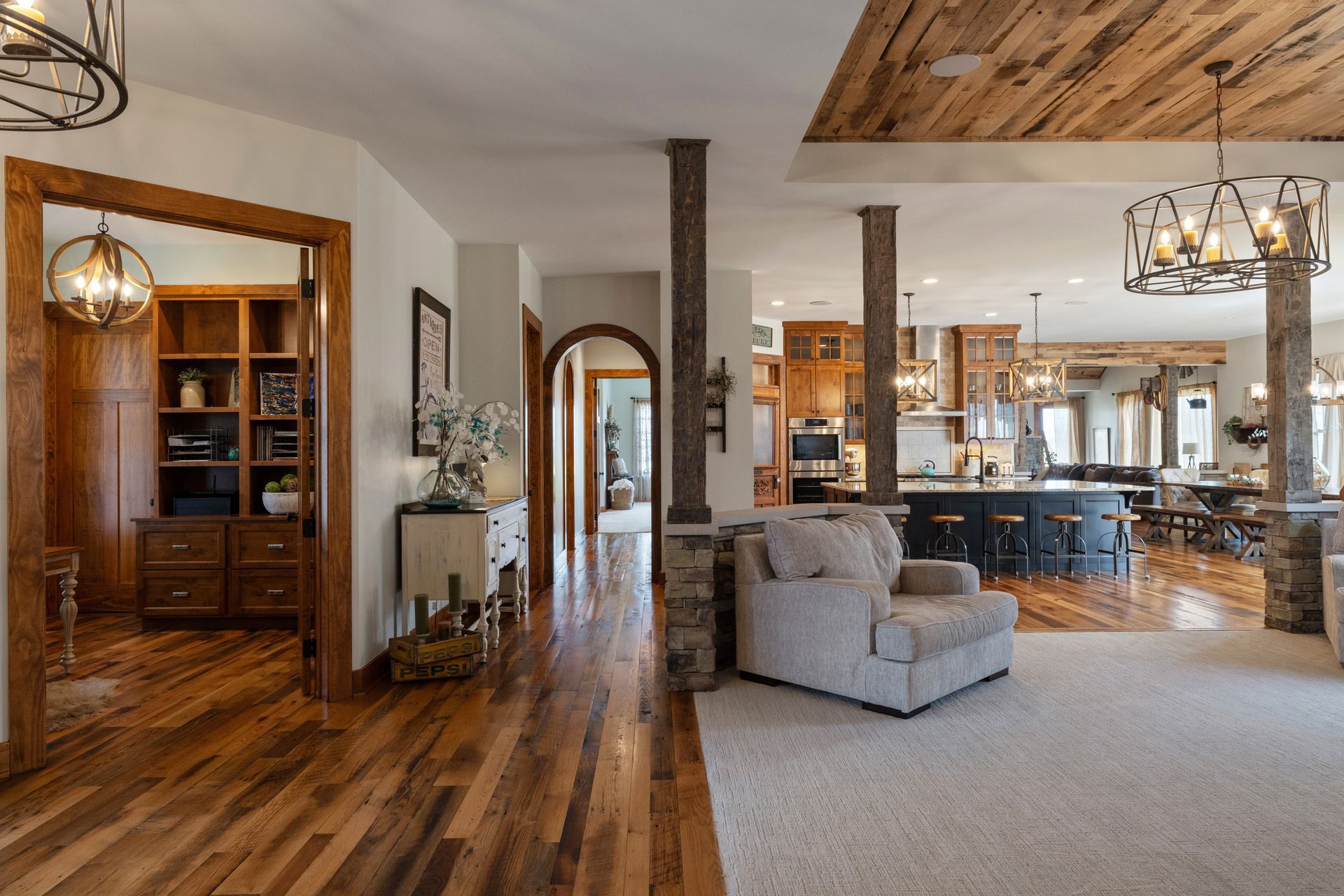 Open-concept home interior with wood floors, light-colored walls, kitchen, living room, and exposed wood beams.