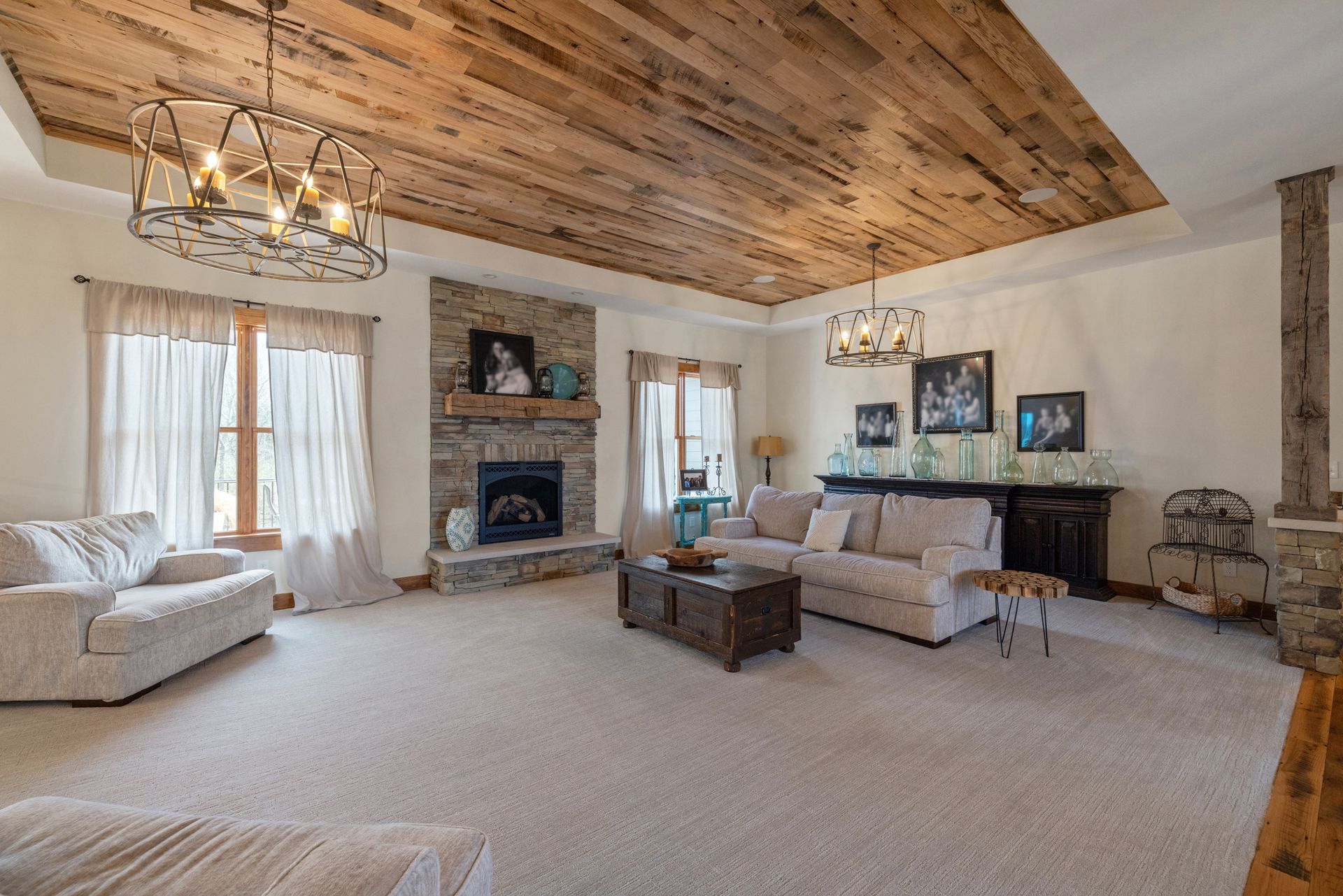 Living room with stone fireplace, wood ceiling, beige furniture, and light carpet.