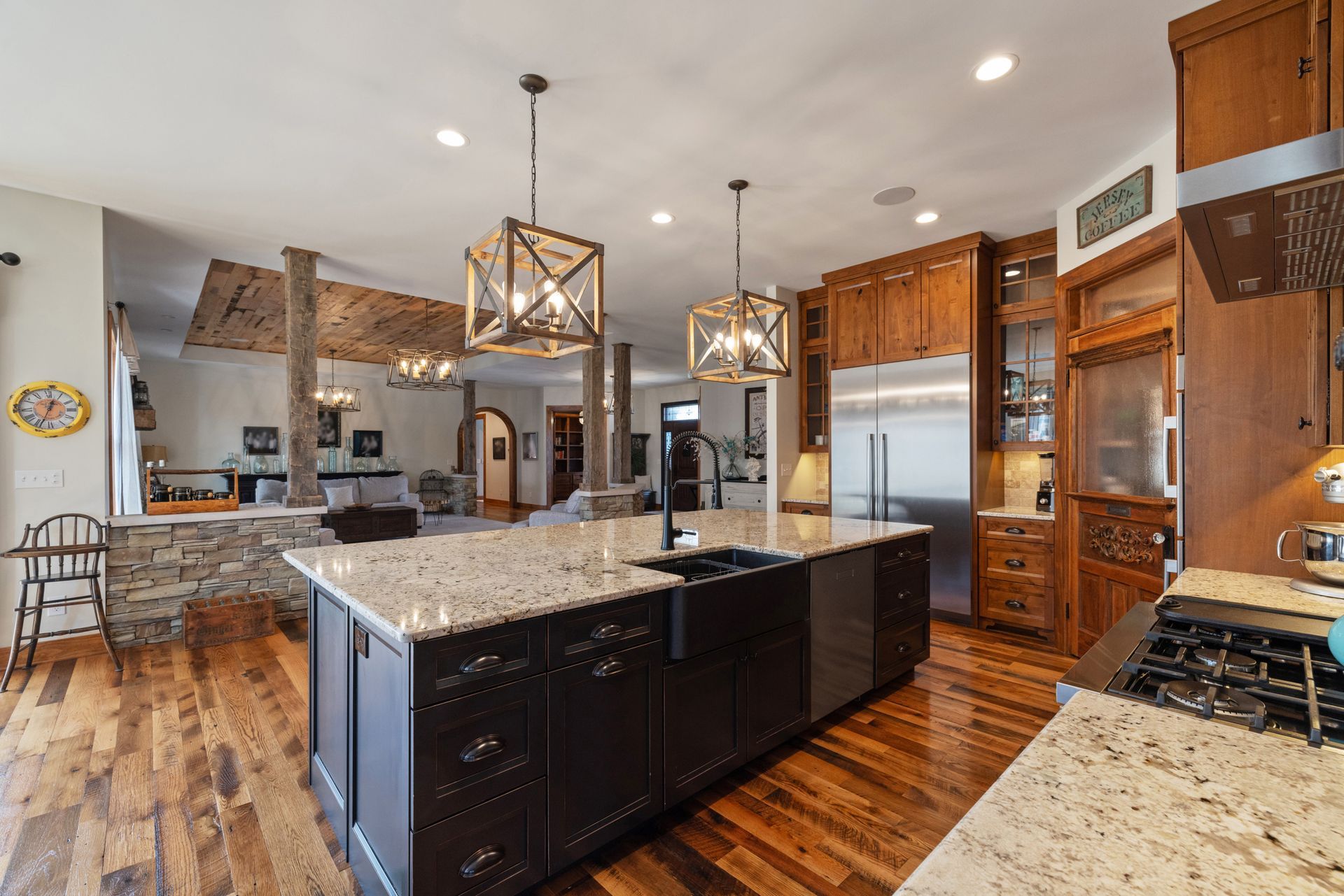 Spacious kitchen with a dark island, granite countertops, and wooden cabinets.  Overhead pendant lights and hardwood floors.