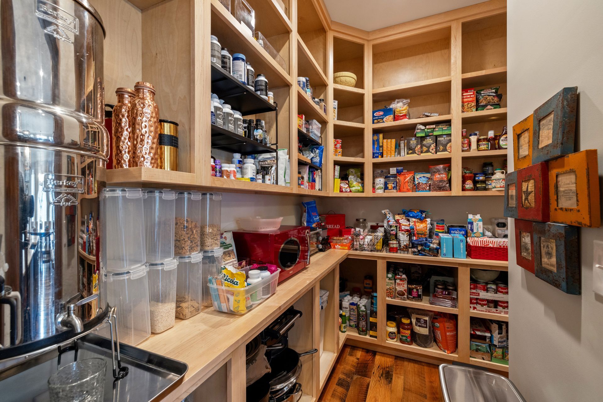 A well-stocked pantry with wooden shelves and various food items, a water filter, and a red appliance.