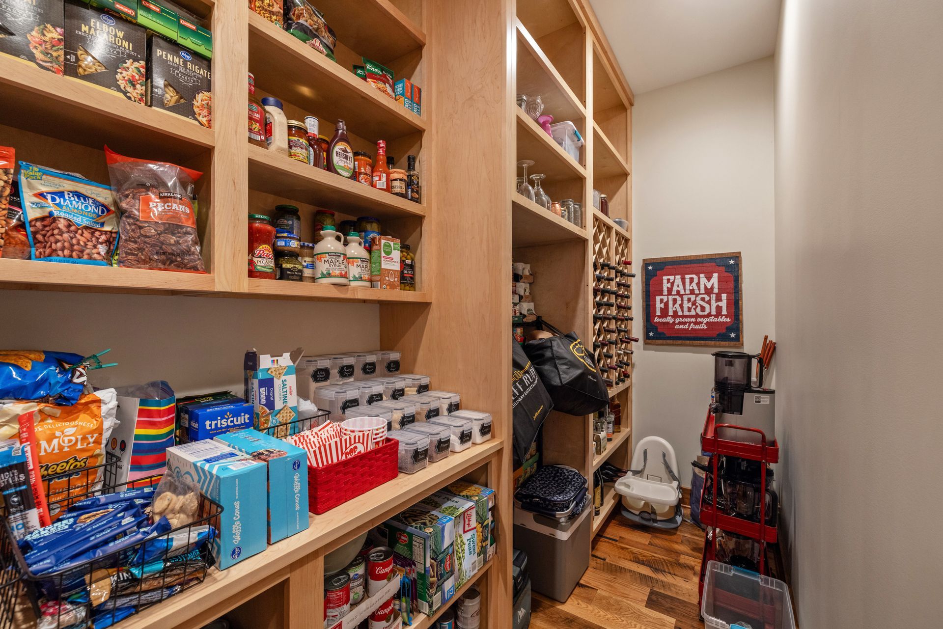 Pantry with shelves stocked with food items and storage, wood flooring. 