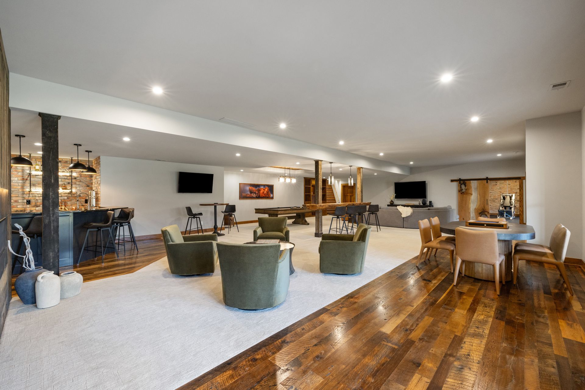 Spacious finished basement with bar, seating areas, pool table, and wood flooring.