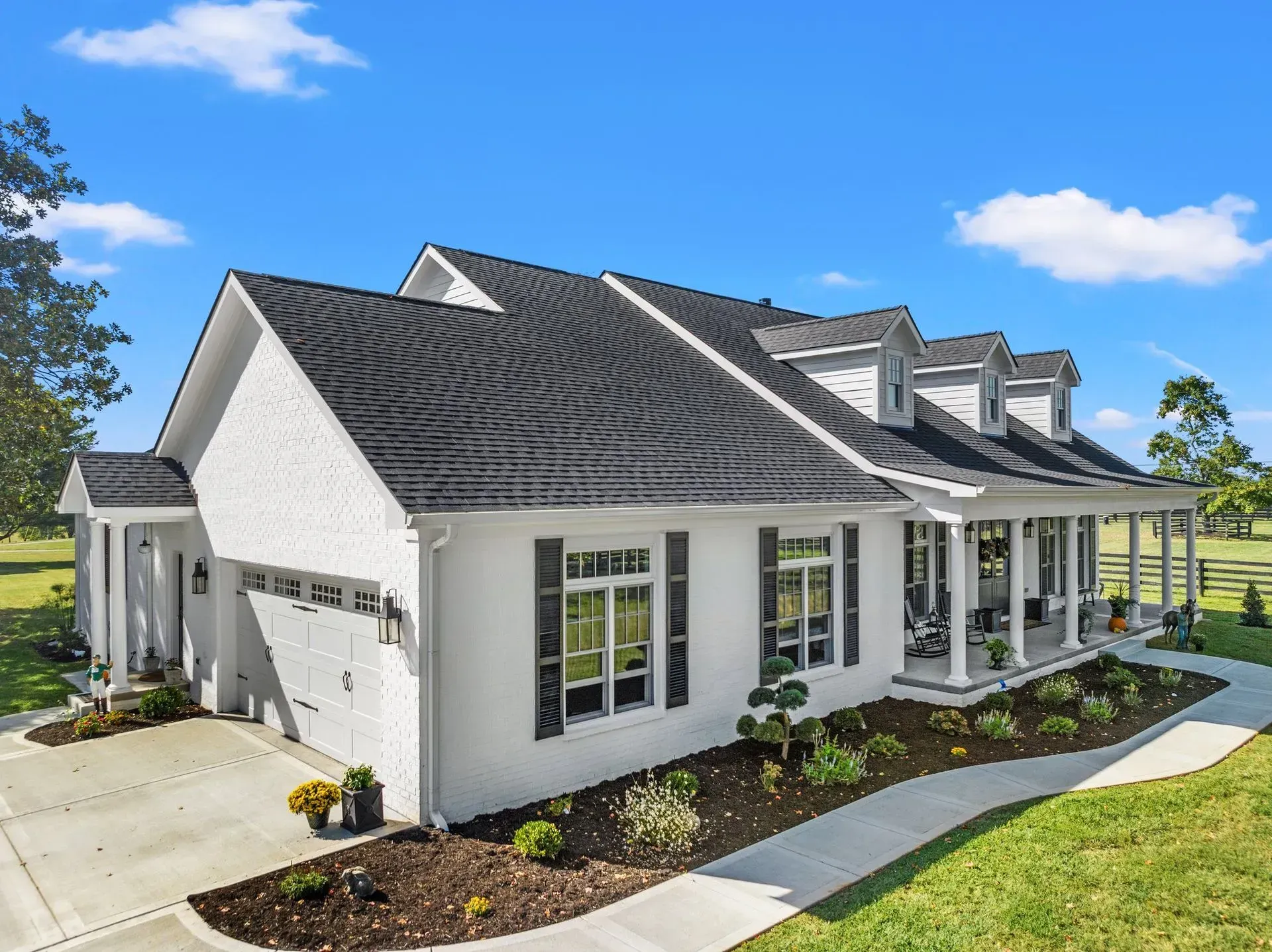 White house with black roof, shutters, and garage door. Green lawn, blue sky.