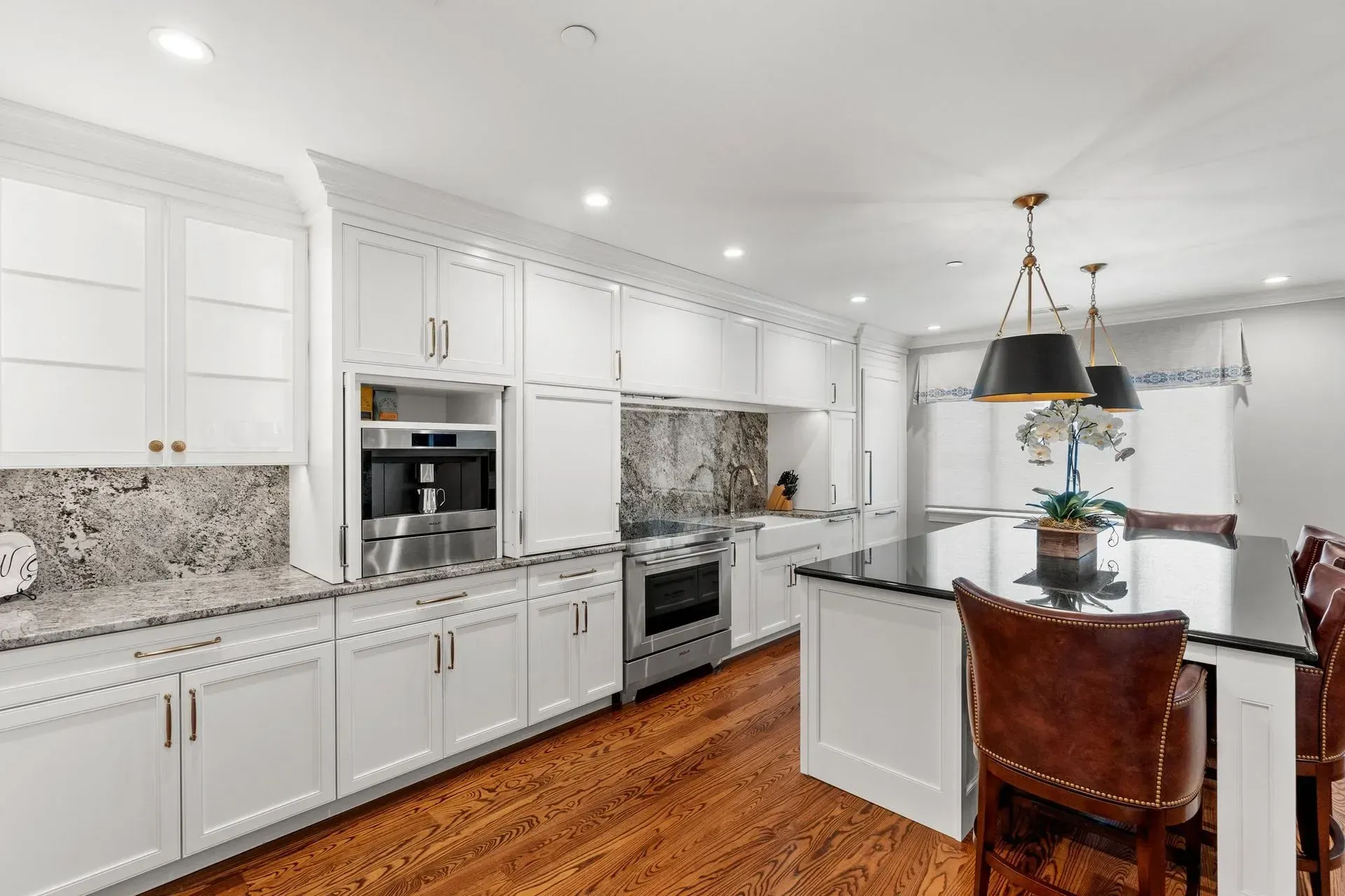 White kitchen with marble backsplash, stainless steel appliances, dark wood floors, and a large island with chairs.